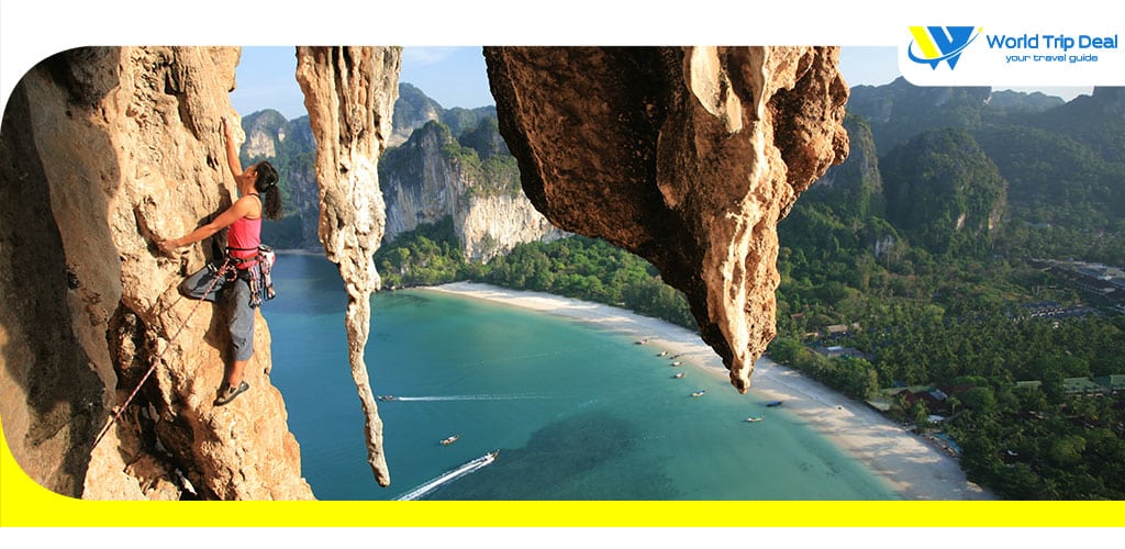 Stunning beautiful professional female rock climber climbing mountain multi pitch in thailand cliff at railay beach cliffs and coconut trees on the background in krabi province – world trip deal